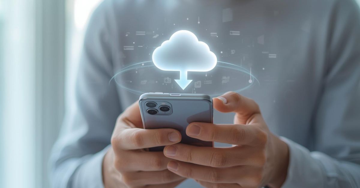 Zbliżenie na dłonie trzymające smartfon, nad którym unosi się delikatna, świecąca ikona chmury, symbolizująca automatyczny backup zdjęć i plików z telefonu do chmury.
